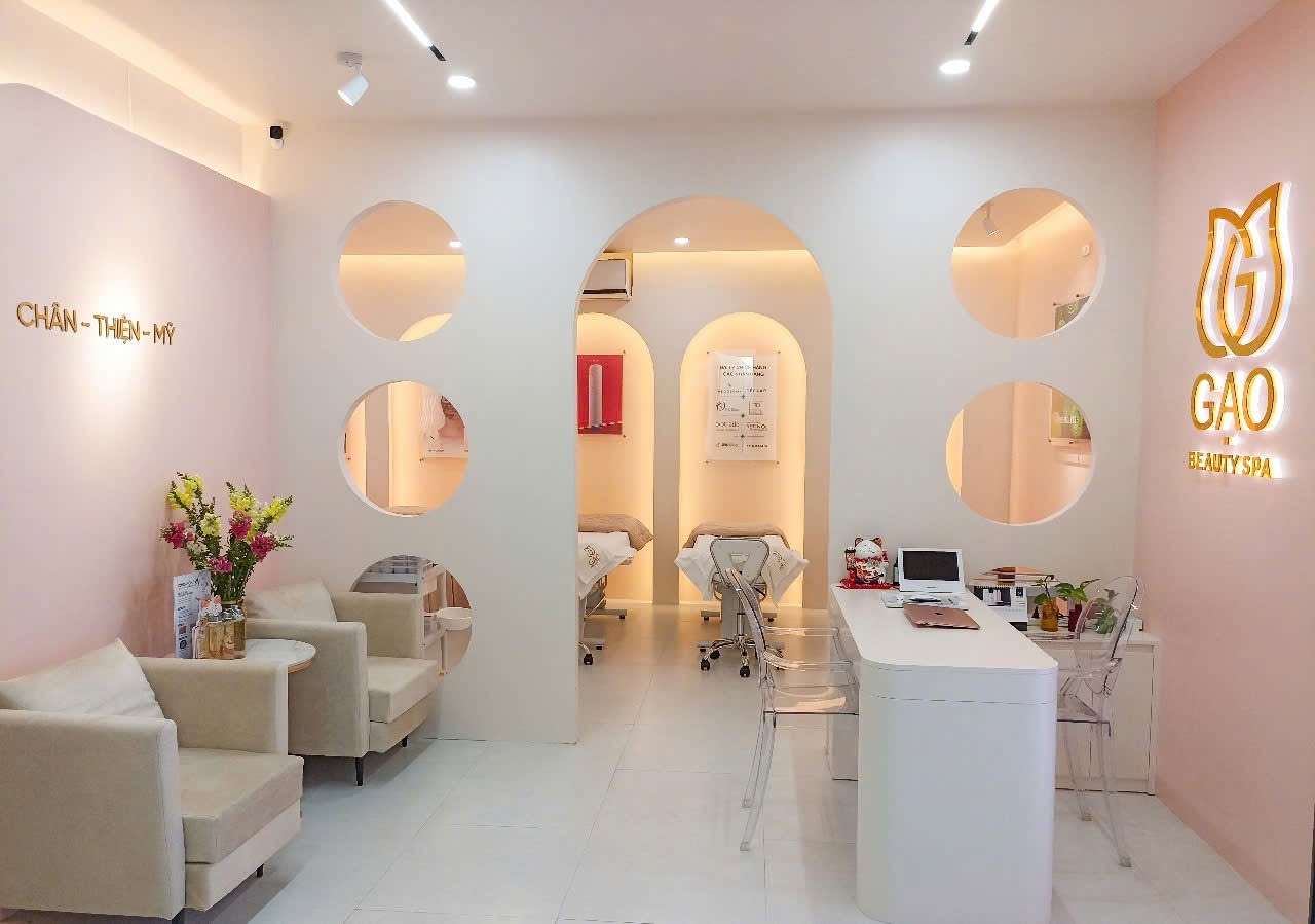 Không gian Gạo Skinlab: tường kem và hồng phấn, cửa vòm lớn cùng các ô tròn, quầy tư vấn trắng, ghế be và logo Gạo vàng kim trên tường.